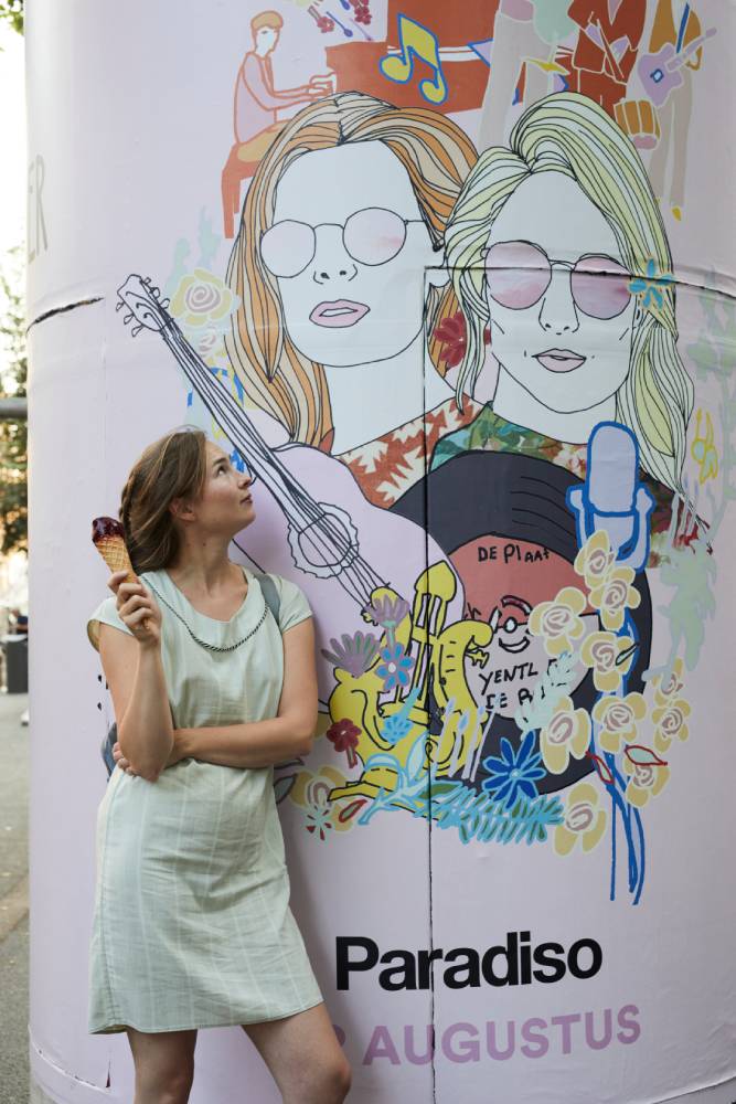 Een foto van Titia naast een poster van haar illustratie op een reclamezuil.